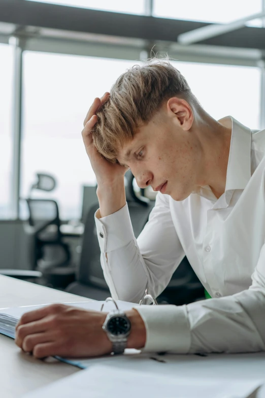 a man sitting at a desk with his head in his hands, a cartoon, trending on pexels, non-binary, a photo of a disheveled man, thin young male, professional picture