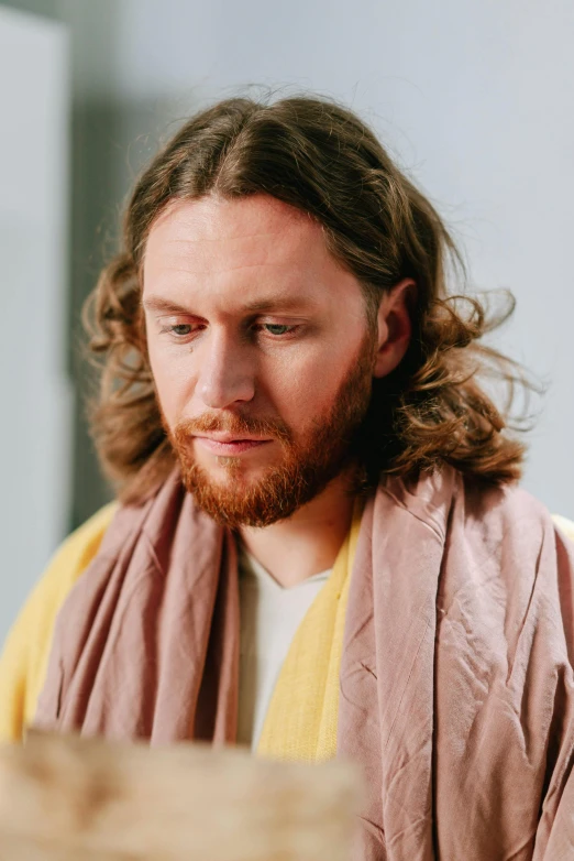 a man with long hair sitting at a table, inspired by Moses van Uyttenbroeck, trending on unsplash, religious robes, wearing a scarf, with yellow cloths, worried