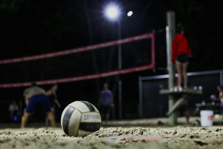 a volleyball ball sitting on top of a sandy beach, at night, profile image, college, lamps on ground