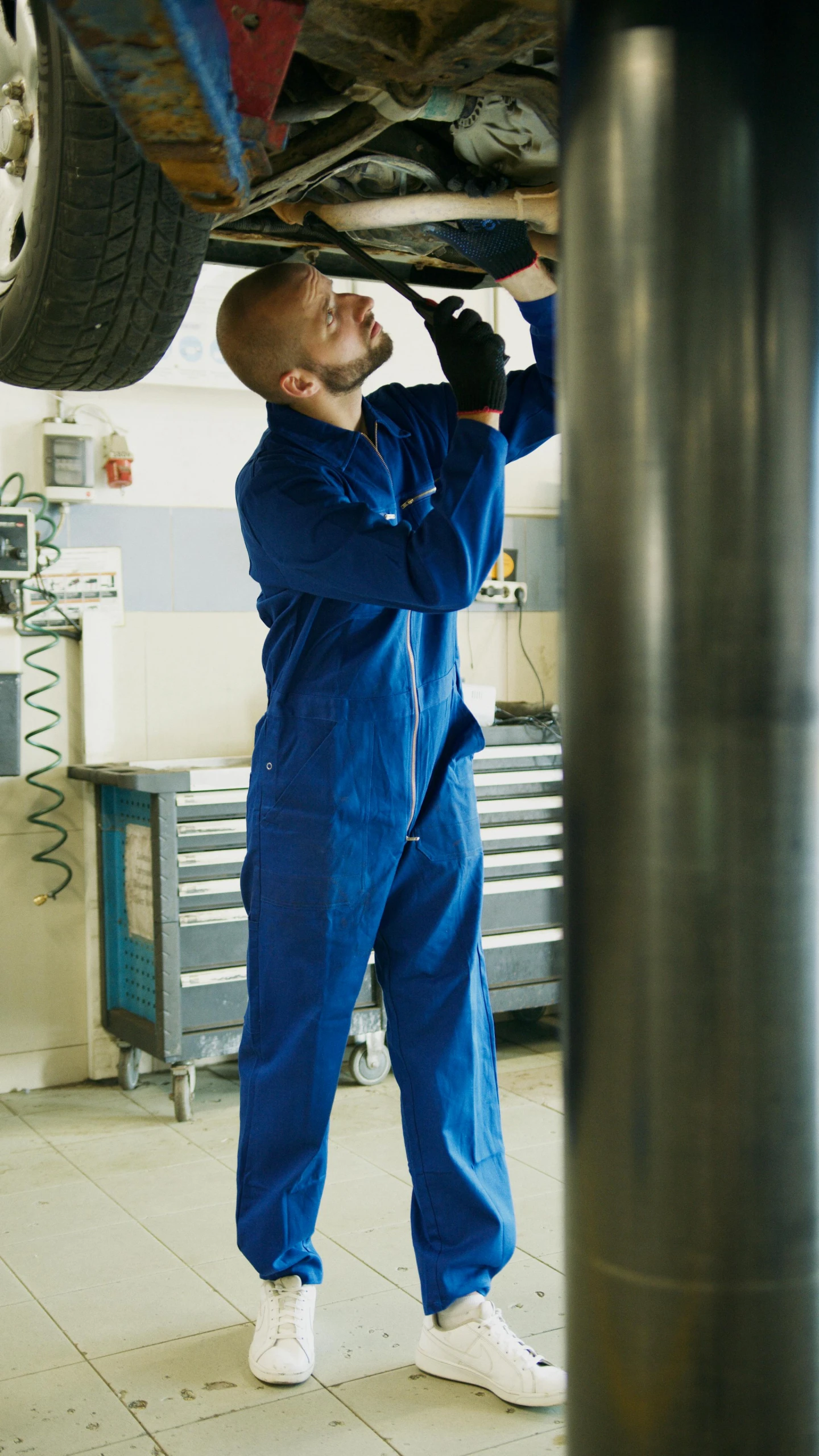 a man working on a car in a garage, by John Murdoch, pexels, wearing human air force jumpsuit, blue surcoat, large tall, praised