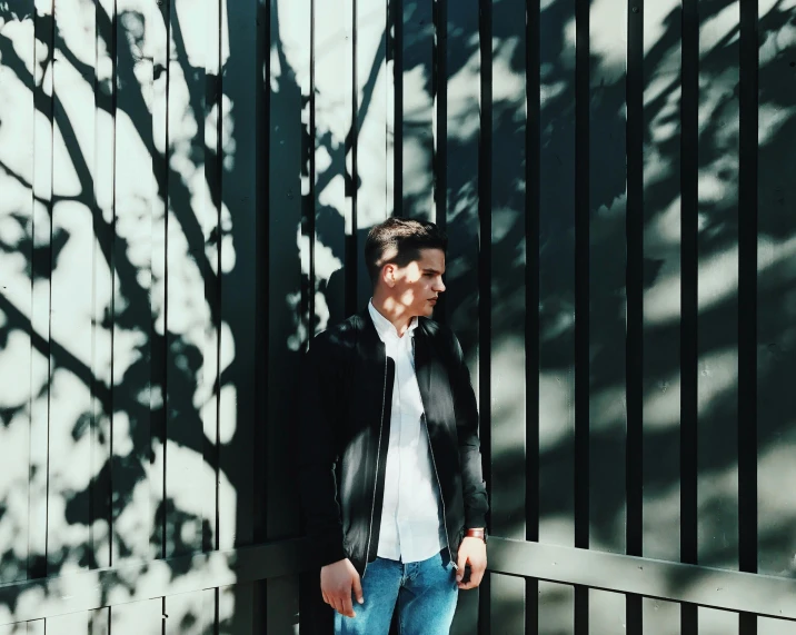a man standing in front of a metal fence, by Niko Henrichon, minimalism, under the soft shadow of a tree, smart casual, lachlan bailey, instagram picture