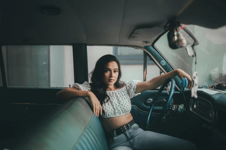 a woman sitting in the driver's seat of a car, a colorized photo, inspired by Elsa Bleda, pexels contest winner, wearing jeans, isabela moner, asian women, wearing a crop top