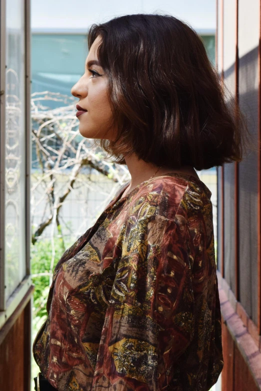 a woman looking out a window at the ocean, an album cover, by Aguri Uchida, unsplash, renaissance, wearing a kurta, paisley, brown short hair, profile pic