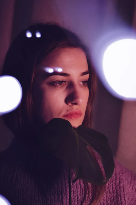 a woman standing in front of a bunch of lights, a picture, inspired by Elsa Bleda, trending on pexels, portrait of depressed teen, led purple eyes, portrait of ana de armas, grainy movie still