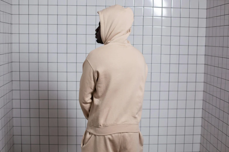 a man standing in front of a urinal in a bathroom, an album cover, by Nina Hamnett, unsplash, beige hoodie, wearing a track suit, 3 / 4 view from back, tonal topstitching