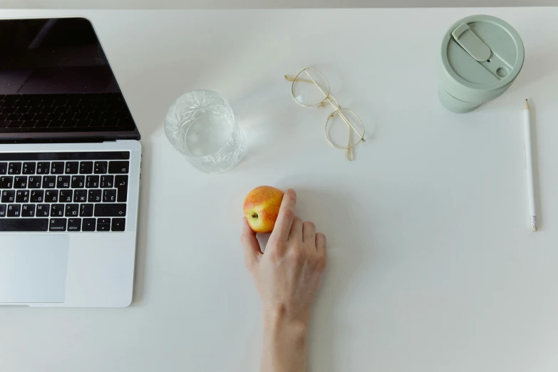 a person eating an apple next to a laptop, a still life, by Carey Morris, trending on pexels, white minimalistic background, background image, back of hand on the table, one object