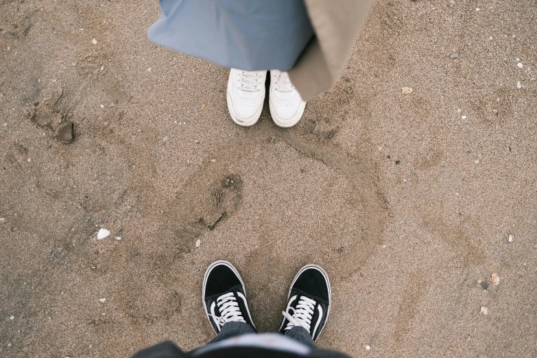 a person standing in the sand with an umbrella, wearing white sneakers, two skinny old people, flatlay, they are close to each other