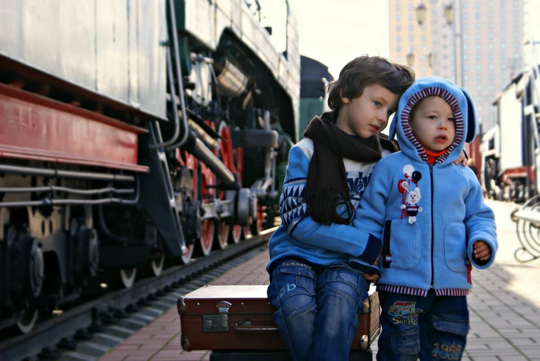 a couple of kids sitting on top of a suitcase, by Lucia Peka, pexels contest winner, steam trains, russian clothes, profile pic, large blue engines