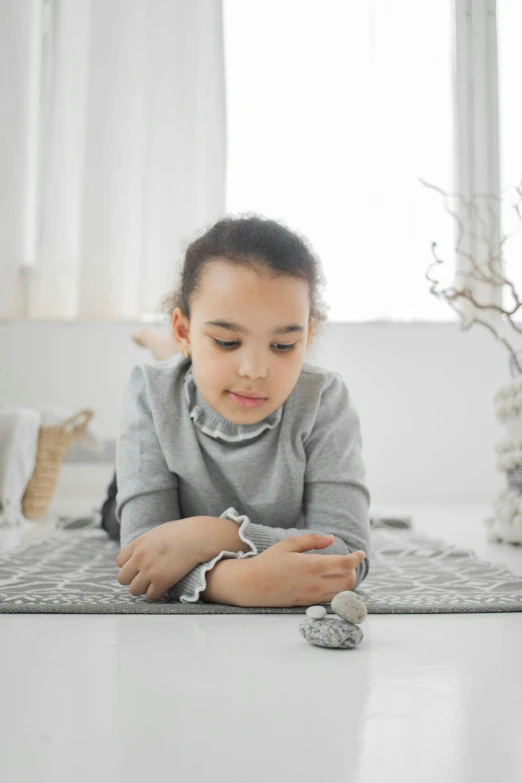 a little girl laying on the floor playing with rocks, by Adam Marczyński, smart textiles, on a table, grey, holding easter eggs