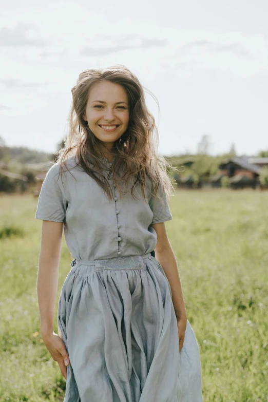 a woman in a blue dress standing in a field, white shirt and grey skirt, wearing farm clothes, sofya emelenko, smiling