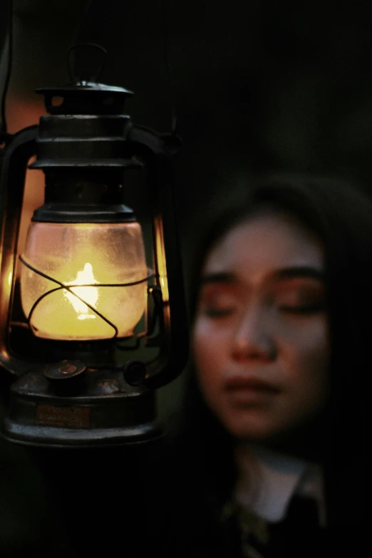 a woman standing next to a lantern with a candle in it, an album cover, inspired by irakli nadar, pexels contest winner, indonesia, pensive expression, ( ( theatrical ) ), close-up photo
