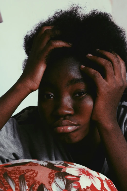 a close up of a person laying on a bed, by Lily Delissa Joseph, trending on unsplash, hyperrealism, black teenage boy, hands in her hair, looking confused, on a gray background