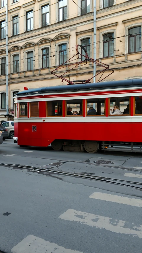 a red train traveling down a street next to a tall building, inspired by István Nagy, pexels contest winner, art nouveau, red brown and grey color scheme, square, cart, intersection