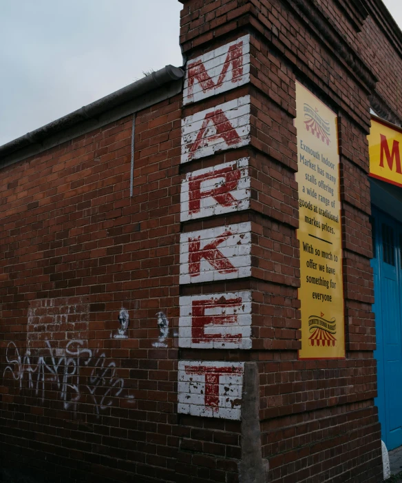 a brick building with graffiti on the side of it, by Kev Walker, pexels, colored market stand, sign, marc, restored