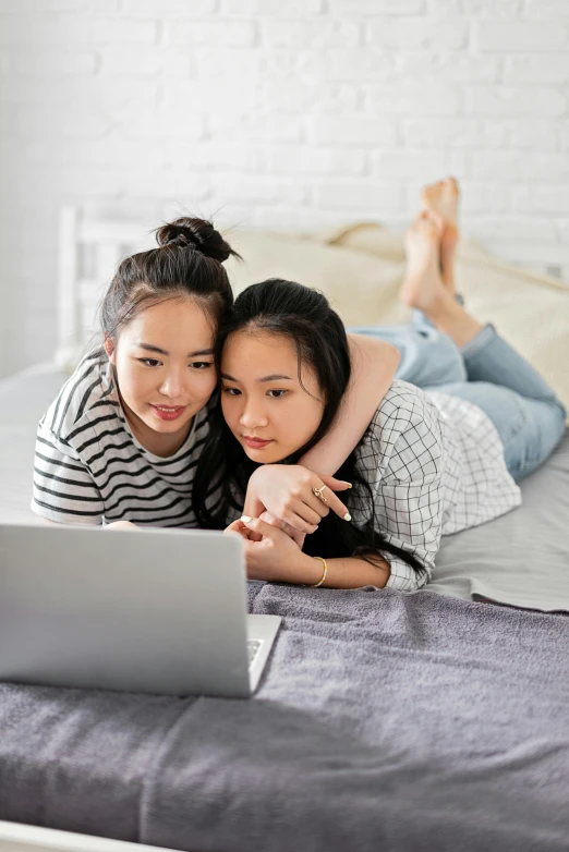 two women laying on a bed looking at a laptop, trending on pexels, asian girl with long hair, square, editors choice, home video