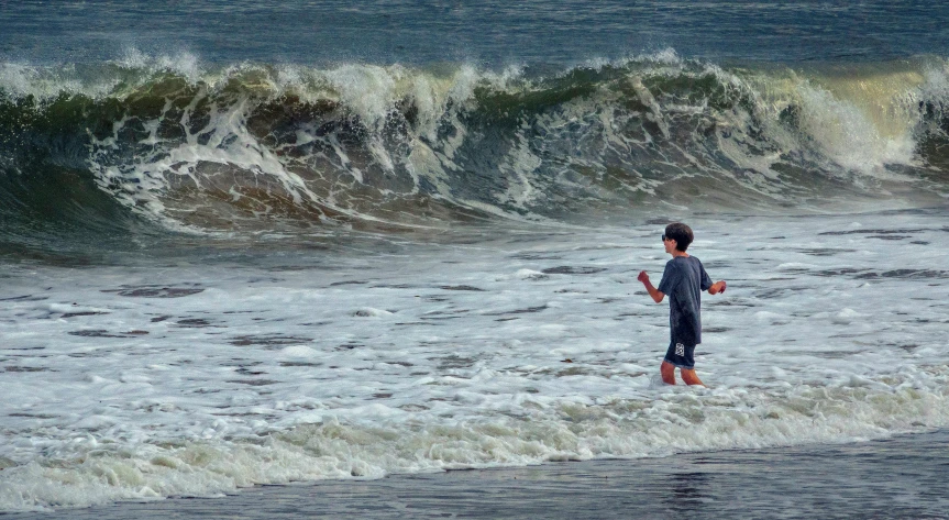 a person standing in the ocean holding a surfboard, currents, kids playing at the beach, tumultuous, trending photo