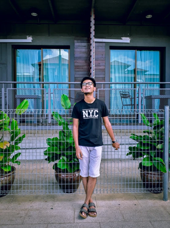 a man standing in front of a metal fence, inspired by Ryan Yee, pexels contest winner, lyco art, wearing shorts and t shirt, vine covered, profile image, full body picture