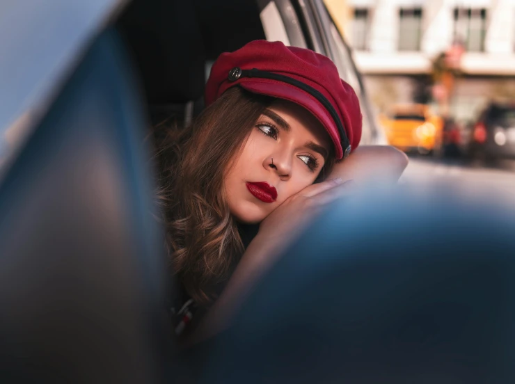 a woman looking out the window of a car, trending on pexels, visual art, an oversized beret, tired expression, crimson themed, girl with brown hair