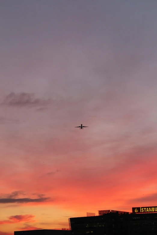 a plane flying over a city at sunset, a picture, by Peter Churcher, minimalism, sherbert sky, silhouette over sunset, sunset sky, looking up onto the sky