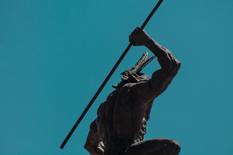 a statue of a man holding a spear on top of a building, unsplash, figuration libre, skilled warrior of the apache, blue sky, zulu, medium close shot