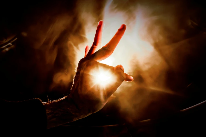 a person holding their hand up in the air, an album cover, by Daniel Lieske, pexels contest winner, art photography, lens flare. occult photorealism, giving the middle finger, fire poi, peace