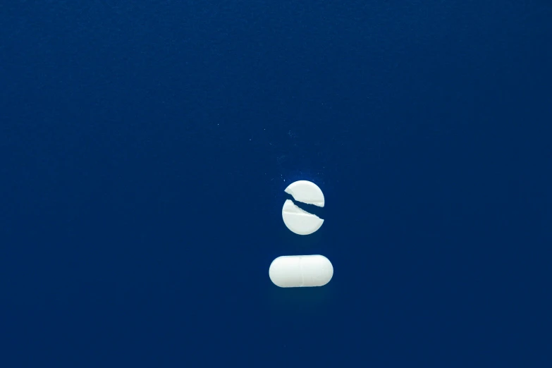 a couple of pills sitting on top of a blue surface, by Elsa Bleda, unsplash, postminimalism, yinyang shaped, middle of the ocean, one blimp in the distance, white: 0.5