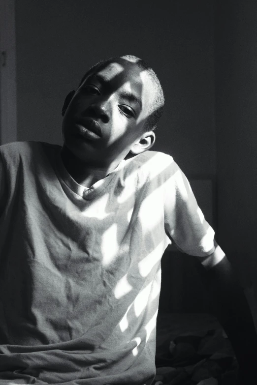 a black and white photo of a man sitting on a bed, an album cover, unsplash, realism, black teenage boy, sun glare, taken in the mid 2000s, shaven face