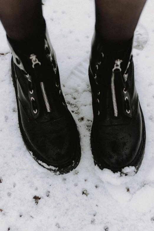 a person standing in the snow wearing black boots, by Andries Stock, trending on pexels, many zippers, creepers, black and silver, made of rubber