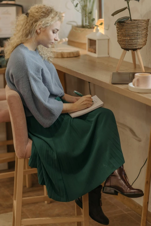 a woman sitting at a desk writing in a notebook, by Eero Järnefelt, trending on pexels, renaissance, teal skirt, sitting on designer chair, wearing a green sweater, designed for cozy aesthetics!