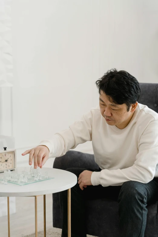 a man sitting on a couch next to a coffee table, inspired by Joong Keun Lee, kinetic art, tabletop game board, with clear glass, akihito tsukushi, on a white table