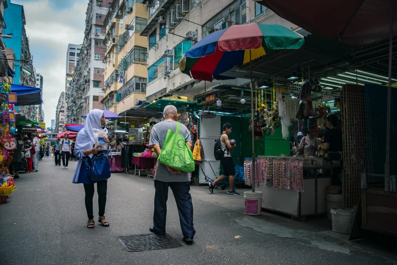 a group of people walking down a street next to tall buildings, wet market street, a man wearing a backpack, canopies, multicoloured