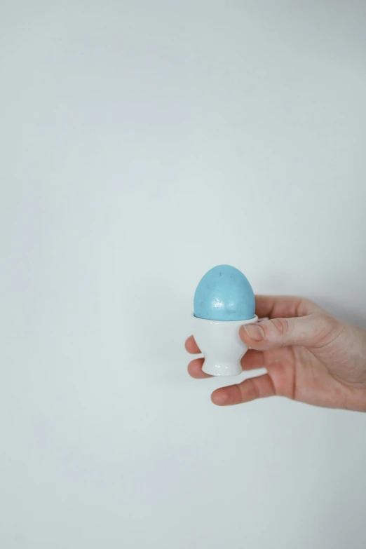a hand holding a blue and white cup, he has a big egg, blue: 0.25, photoshoot, brushed white and blue paint