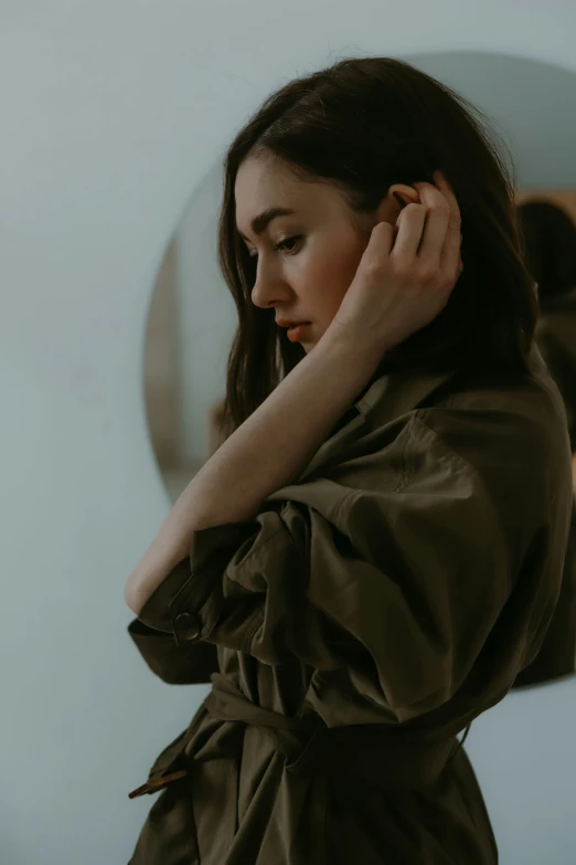 a woman standing in front of a mirror, inspired by Elsa Bleda, trending on pexels, green and brown clothes, thoughtful pose, desaturated, arm around her neck
