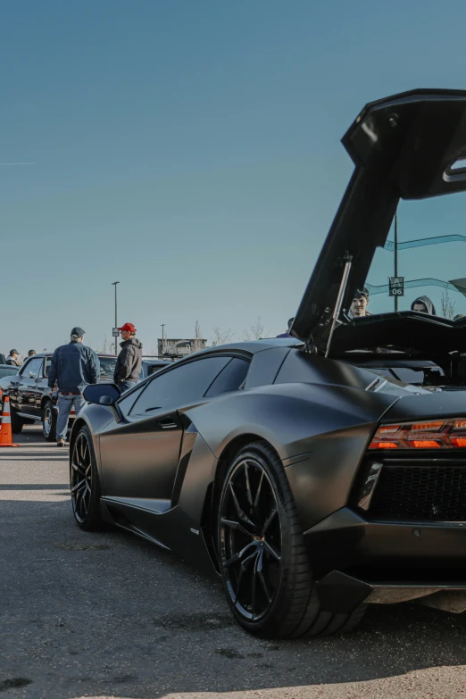 a black sports car parked in a parking lot, a picture, unsplash, happening, veneno, lots of people, performance, january 20th