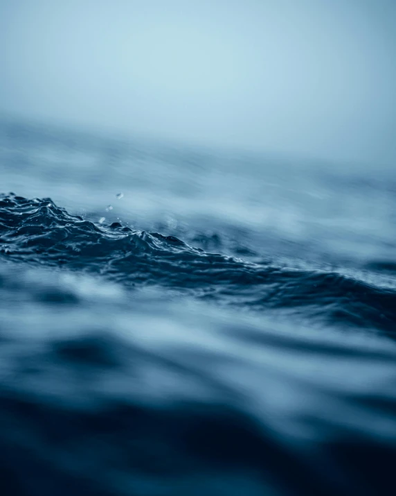 a close up of a body of water with waves, somber mood, looking off to the side, blue blurred, very wet