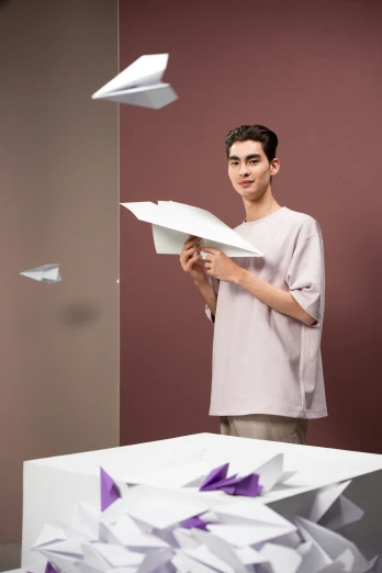 a man standing in front of a pile of papers, inspired by jeonseok lee, trending on unsplash, paper airplane, wearing a light shirt, non binary model, catalog photo
