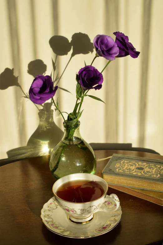 a cup of tea and a book on a table, inspired by Violet Fuller, translucent roses ornate, sun puddle, color photograph, taken in the early 2020s