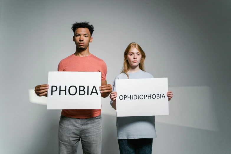 a man and a woman holding signs that say phobia, a photo, trending on unsplash, antipodeans, on a gray background, oblivion, high school, people