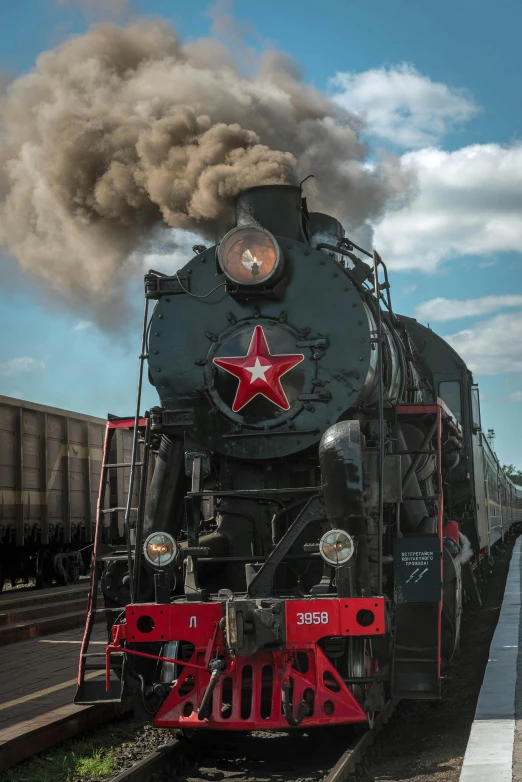 a train traveling down train tracks next to a train station, a portrait, by Ihor Podolchak, pexels contest winner, socialist realism, black shirt with red star, large blue engines, steam clouds, 15081959 21121991 01012000 4k