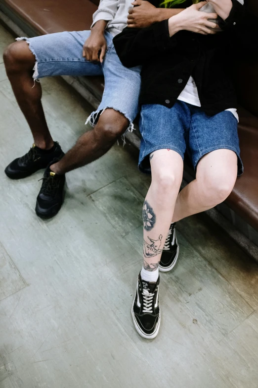 a couple of men sitting next to each other on a bench, a tattoo, by Carey Morris, trending on pexels, jean shorts, in a subway, non binary model, legs intertwined