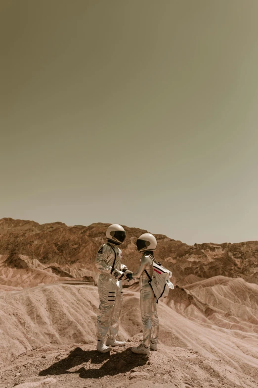 a couple of astronauts standing on top of a dirt field, a colorized photo, trending on unsplash, romanticism, red sea, calmly conversing 8k, slightly pixelated, sepia photography