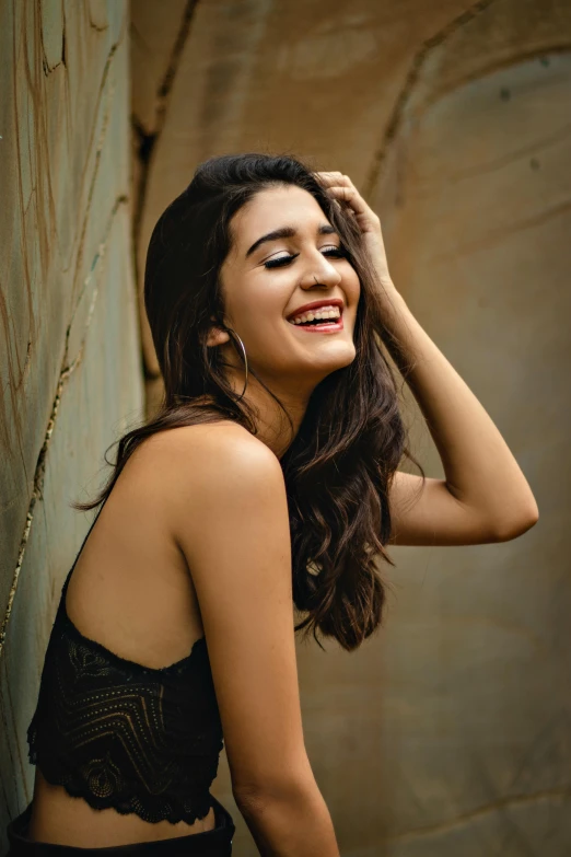 a woman standing next to a wall with a smile on her face, trending on pexels, happening, maya ali mage, hair, square, concert