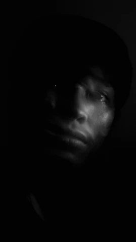 a black and white photo of a man in the dark, inspired by Gordon Parks, digital art, ( ( dark skin ) ), hud face, found footage video, peaceful expression