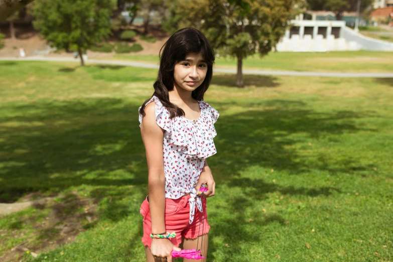 a young girl standing on top of a lush green field, instagram, dora the explorer as real girl, at a park, student, official photo