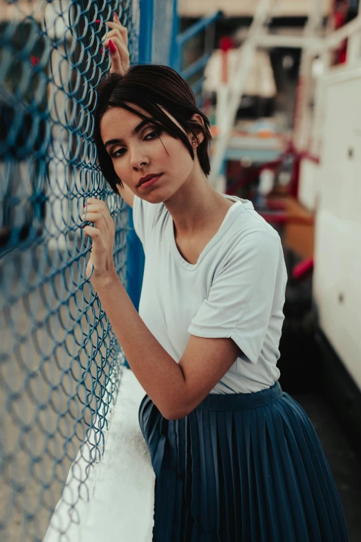 a woman leaning against a chain link fence, inspired by Elsa Bleda, pexels contest winner, portrait emily ratajkowski, on a boat, alanis guillen, dressed in a white t-shirt