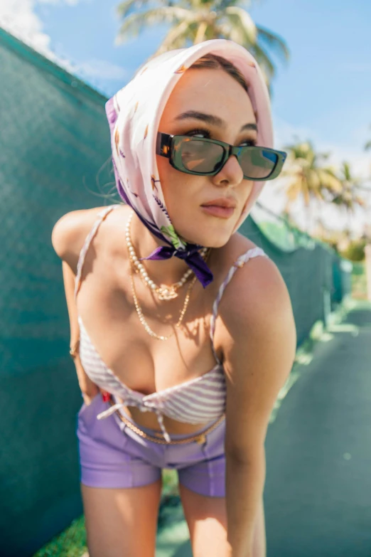 a woman standing on top of a tennis court holding a racquet, an album cover, by Marshall Arisman, trending on pexels, purple halter top, wearing a head scarf, bad bunny, attire: bikini