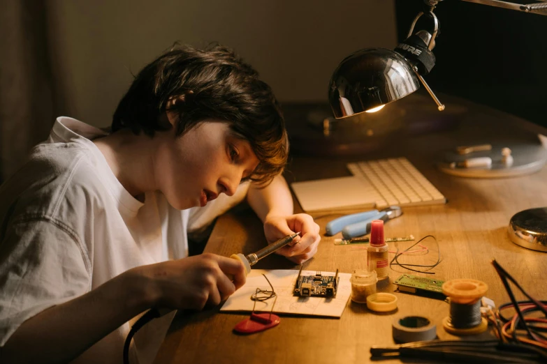 a boy sitting at a desk working on a project, trending on pexels, intricate electronics, with electric arc devices, thumbnail, portrait of a small