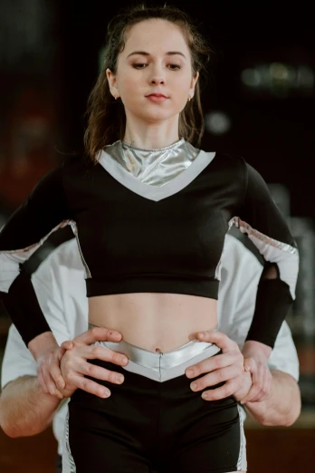 a woman standing with her hands on her hips, an album cover, by Adam Marczyński, trending on pexels, holography, sport bra and shirt, arabian wrestling woman, silver garment, with shoulder pads