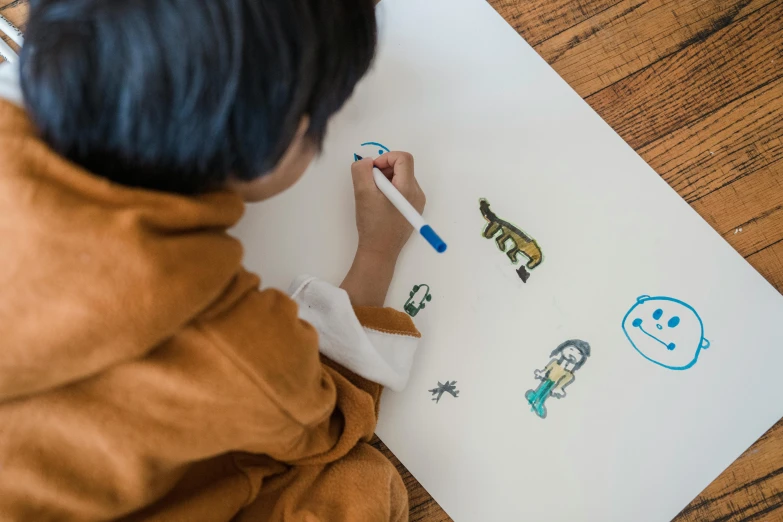 a young boy is drawing on a piece of paper, a child's drawing, by Emma Andijewska, pexels contest winner, manga drawing, stickers illustrations, full body drawing, a high angle shot