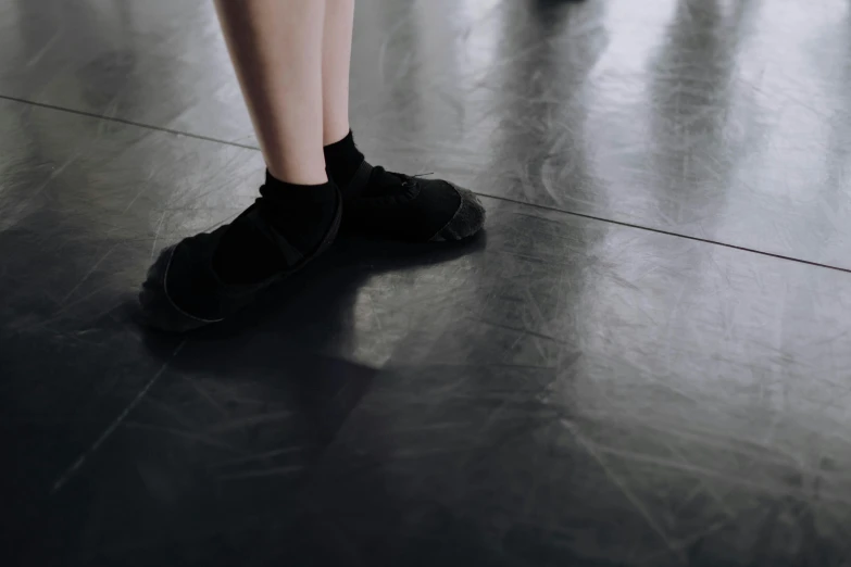 a person standing on top of a black floor, by Elizabeth Polunin, pexels contest winner, gray shorts and black socks, standing in class, made of rubber, from the distance